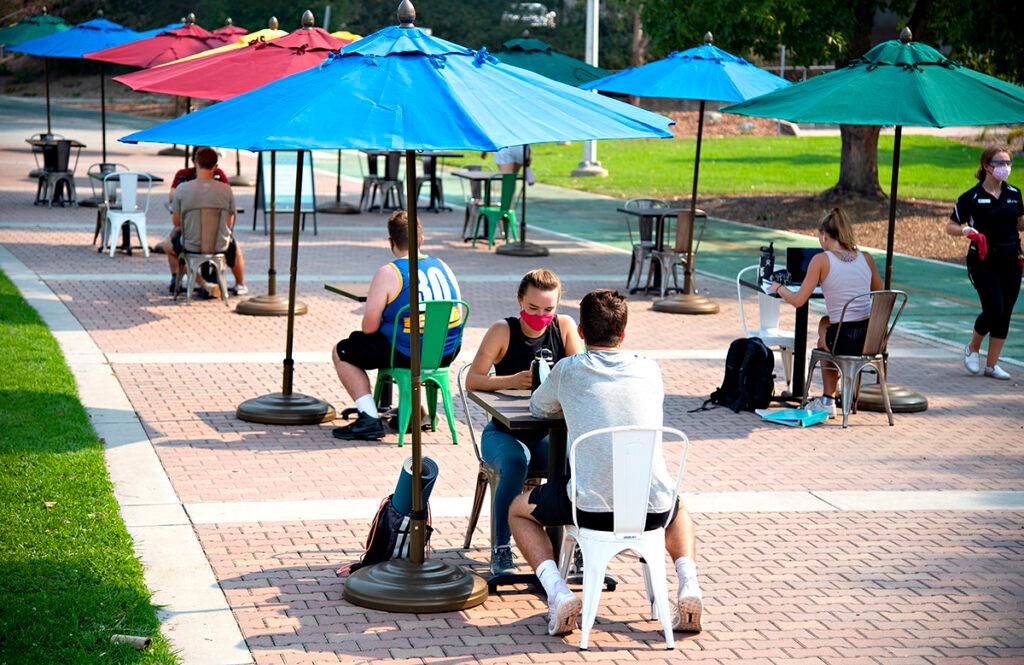 Students sitting at tables with umbrellas