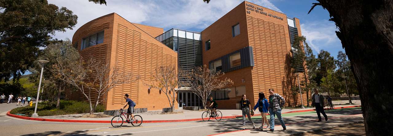 Students and faculty walk and bike outside the Warren J. Baker Center for Science and Mathematics, a modern brick academic building on a sunny day at Cal Poly.