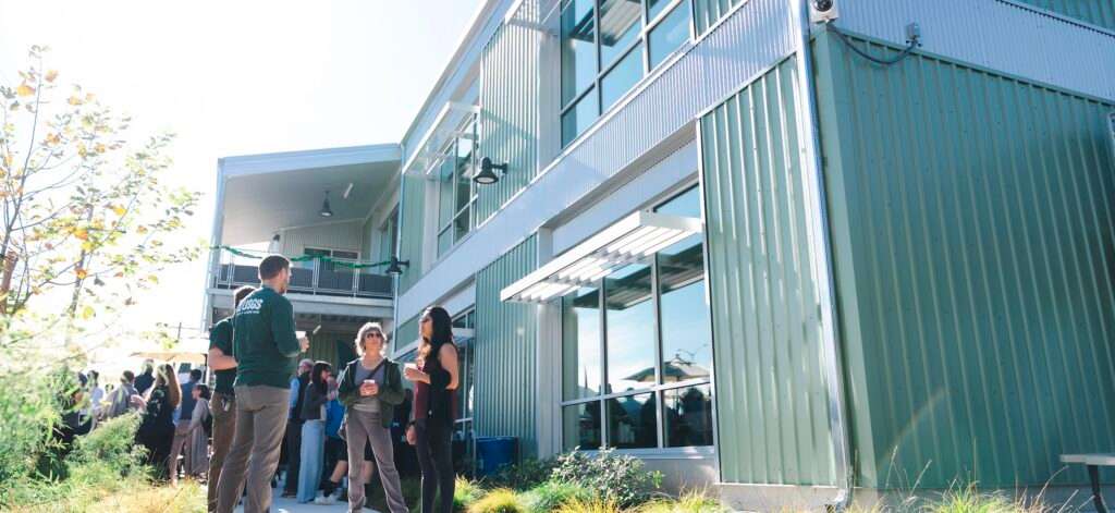 A USGS representative speaks with two attendees outside a modern green metal building.